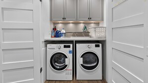 A compact laundry room with two front-loading washing machines, a drying rack, and a shelf with cleaning supplies. - Tranquil Garden Level Retreat near UBC & Airport (Vancouver)