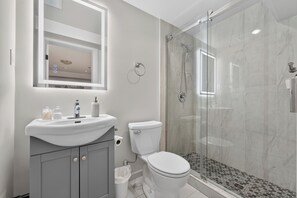 Uma casa de banho moderna com cabine de duche em vidro, lavatório branco com espelho em cima e sanita.