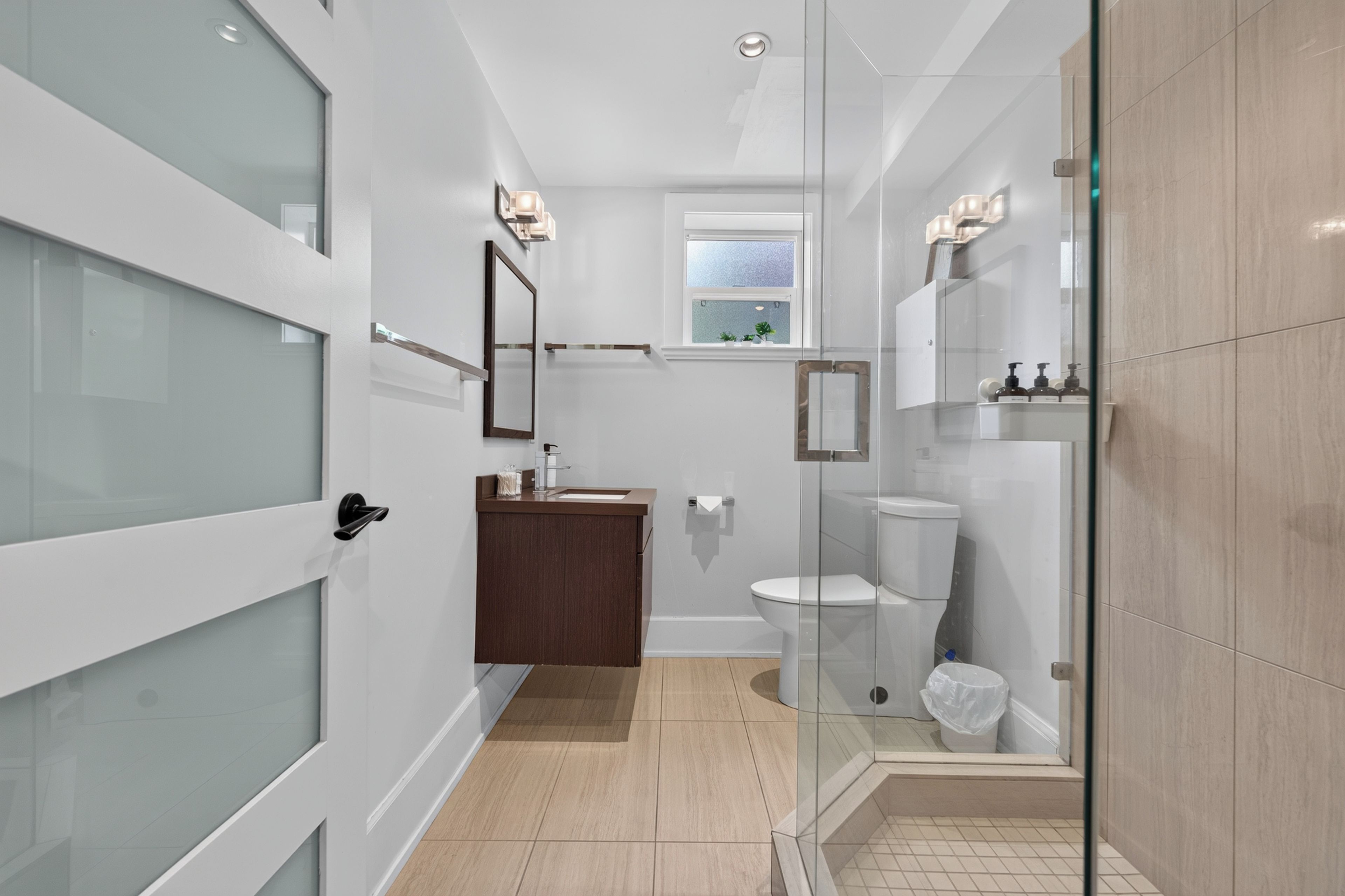 A modern bathroom with a glass shower enclosure, a toilet, and a vanity with a mirror.