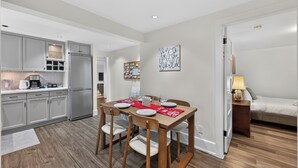 A modern kitchen with grey cabinets, a stainless steel refrigerator, and a dining area with a wooden table and chairs. - Tranquil Garden Level Retreat near UBC & Airport (Vancouver)