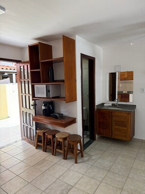 A compact kitchen with a built-in microwave, a coffee maker, and a wooden cabinet with a mirror above the sink. There are three wooden stools at a small table. - Village of the Woods 31 (Porto Seguro)