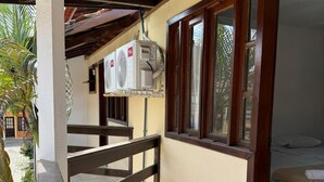Ein Balkon mit Holzgeländer, ein Bett mit weißer Bettdecke und eine an der Wand montierte Klimaanlage.