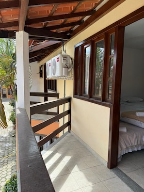 A balcony with a wooden railing, a bed with a white bedspread, and an air conditioning unit mounted on the wall. - Village of the Woods 31 (Porto Seguro)