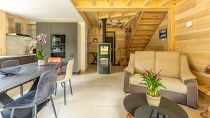 Um interior moderno com área de refeições, cozinha e sala de estar, apresentando vigas de madeira e uma escada.