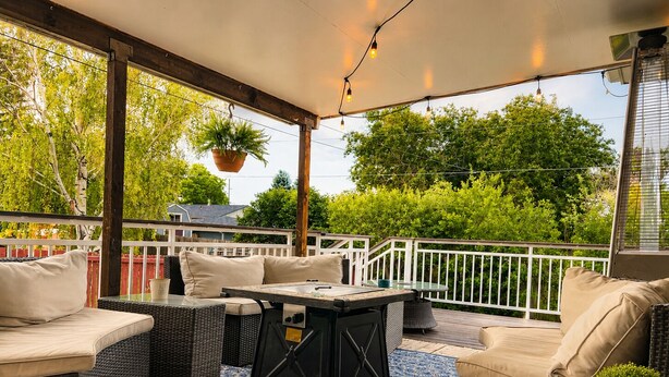 An outdoor patio with wicker furniture, a glass table, and hanging plants.
