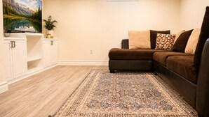 A living room with a sectional sofa, a flat-screen TV, a decorative rug, and a window with a view of the outdoors.