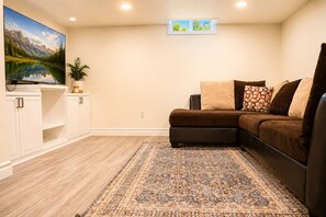 Un salón con un sofá modular, un televisor de pantalla plana, un tapete decorativo y una ventana con vistas al exterior.