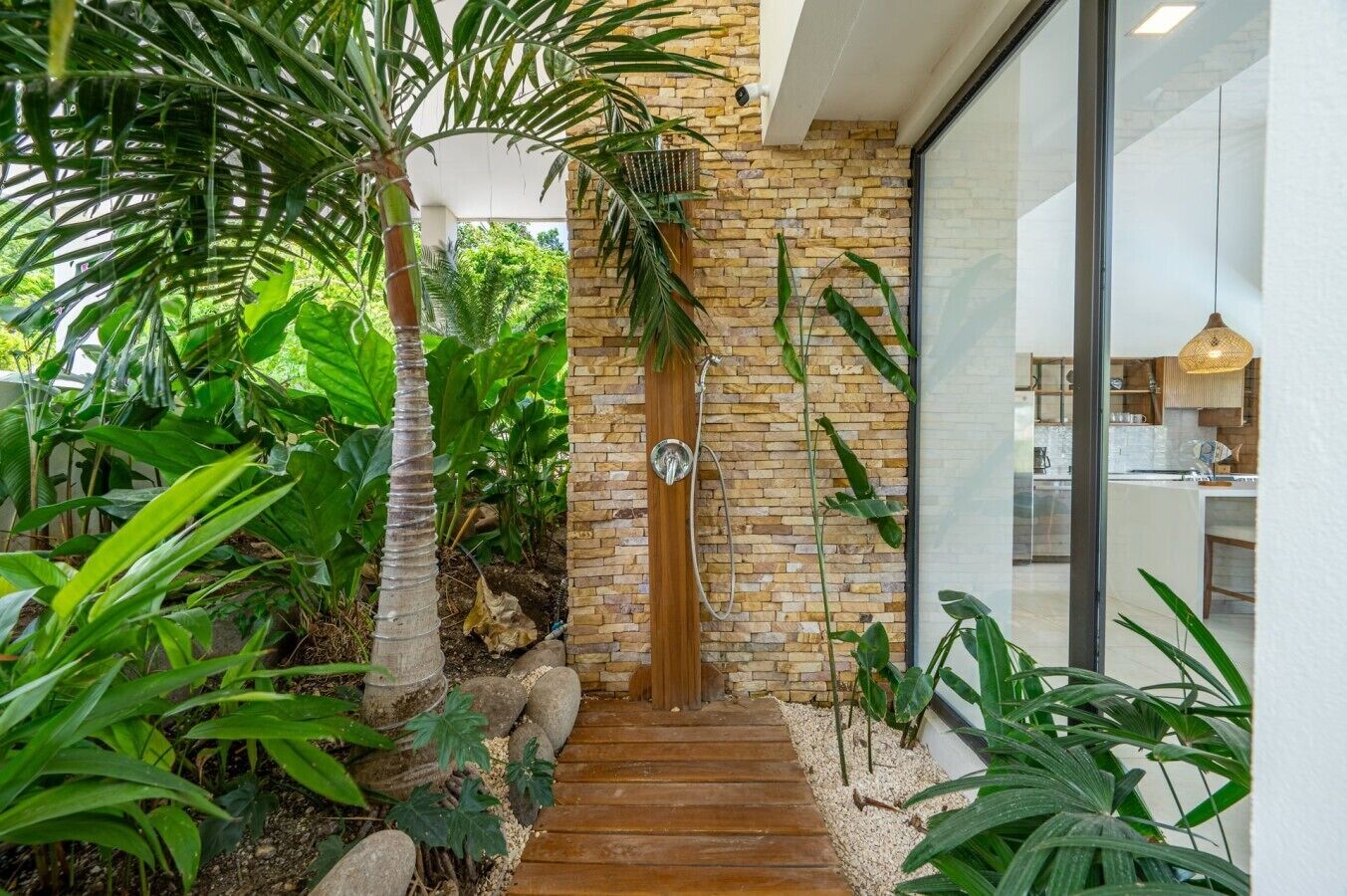 Ein modernes Haus mit einer Holztreppe, die zu einer Backstentür führt, umgeben von üppigem Grün.