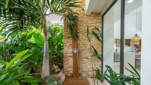 Une maison moderne avec un escalier en bois menant à une porte en briques, le tout entouré d’une végétation luxuriante.