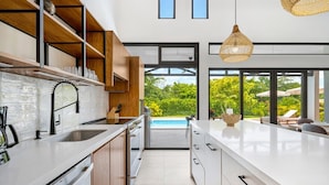 Une cuisine moderne dotée d’un grand îlot central, d’appareils électroménagers intégrés et offrant une vue sur une piscine.