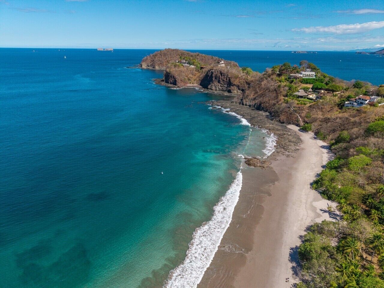 Eine Küstenlandschaft mit Strand, Felsformationen und verstreuten Gebäuden.