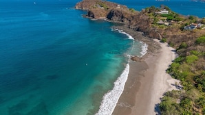 Un paysage côtier avec une plage, des affleurements rocheux et quelques bâtiments dispersés.