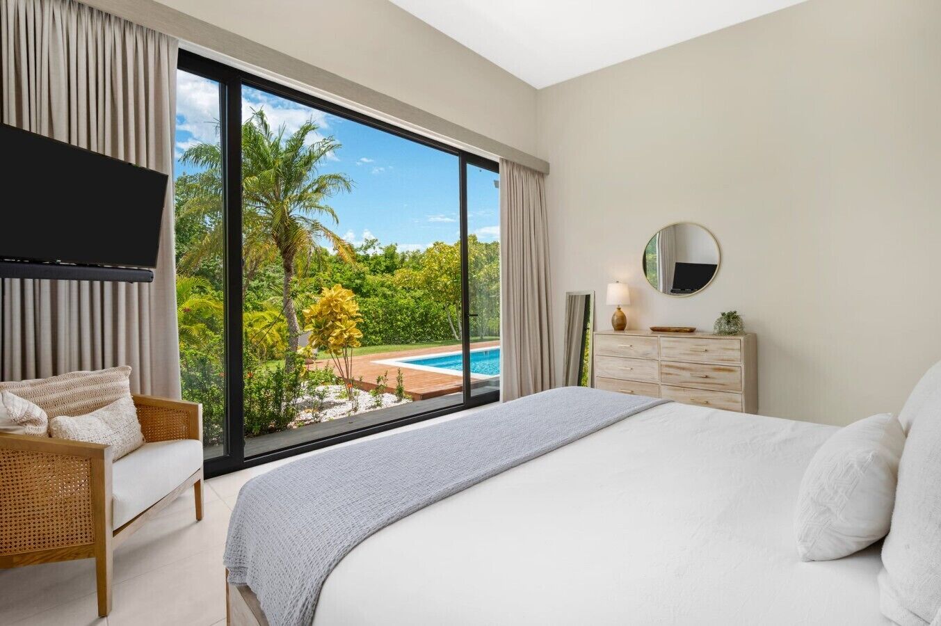 Une chambre avec un grand lit, une télévision, une commode et une vue sur une piscine.