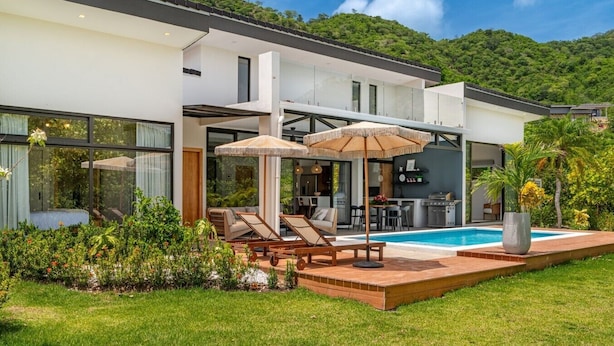 Une maison moderne dotée d’une piscine, d’un espace extérieur aménagé et d’un coin cuisine.