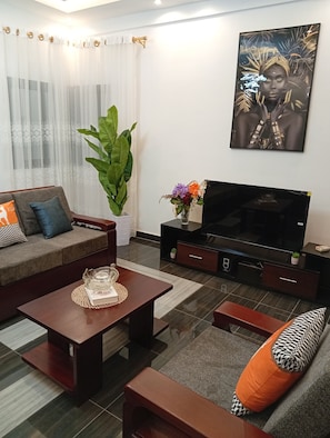 Un salón con sofá, mesa de centro, mueble para televisor y una planta grande.