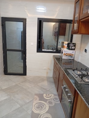Una cocina con estufa a gas, armarios, refrigerador y ventana con vistas al exterior.