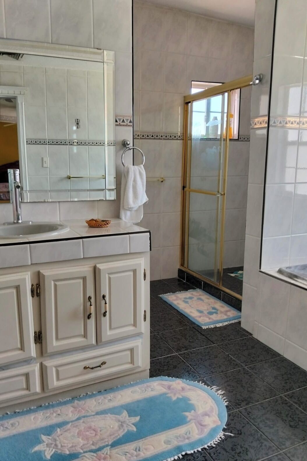 Une salle de bain équipée d’un lavabo, d’un miroir, de placards, d’une douche et d’un tapis à motifs.