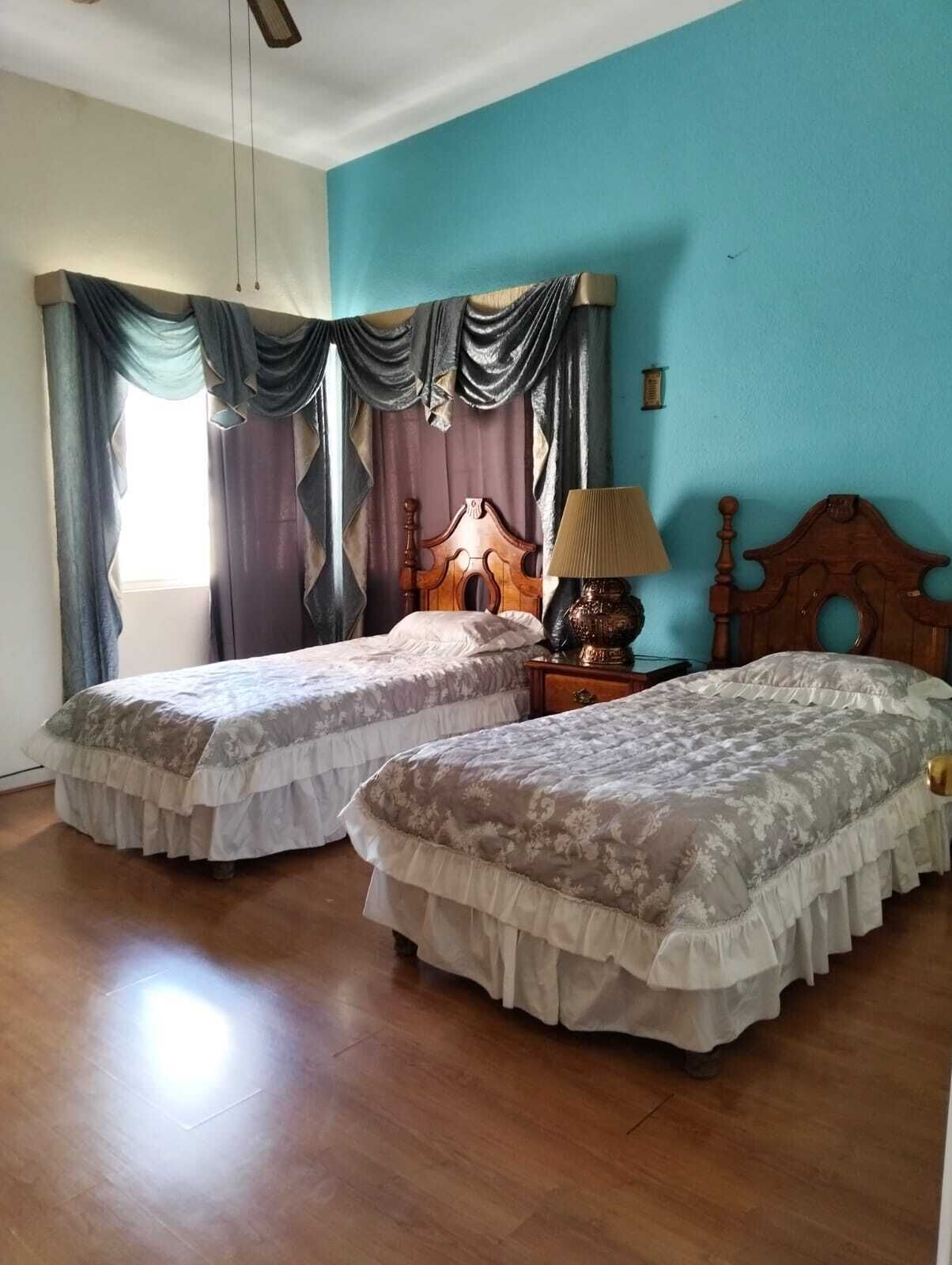 A room with two beds, a nightstand, a lamp, and a window with curtains.