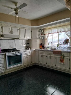 A kitchen with white cabinets, a stove, a sink, and a ceiling fan.