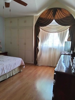 Um quarto com uma cama, cômoda, guarda-roupa e janela com cortinas.