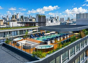 A rooftop pool area with lounge chairs and a hot tub, surrounded by greenery and overlooking a cityscape. - Nawi Beachfront Escape Apartment - Pool, Gym & Ocean Access (João Pessoa)