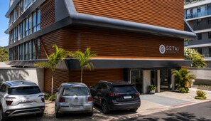 Um edifício moderno com a placa 'SETAI AQUAMARIS'. Três carros estacionados na frente.