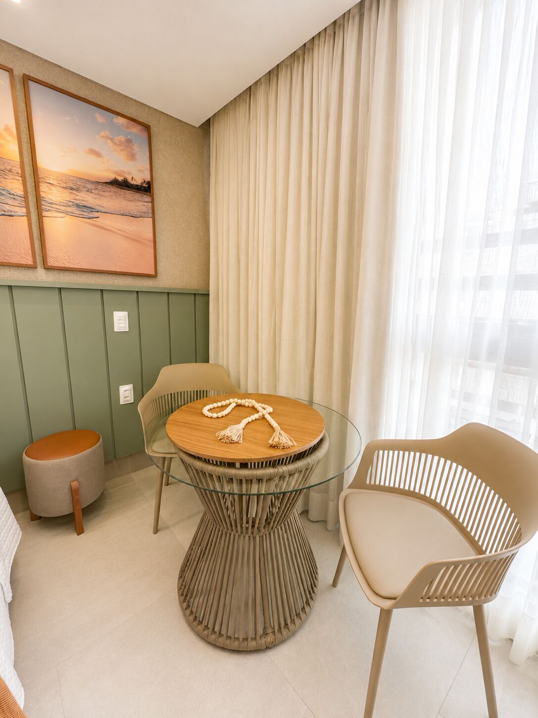A room with a round glass table, two chairs, a small stool, and a wall-mounted picture.