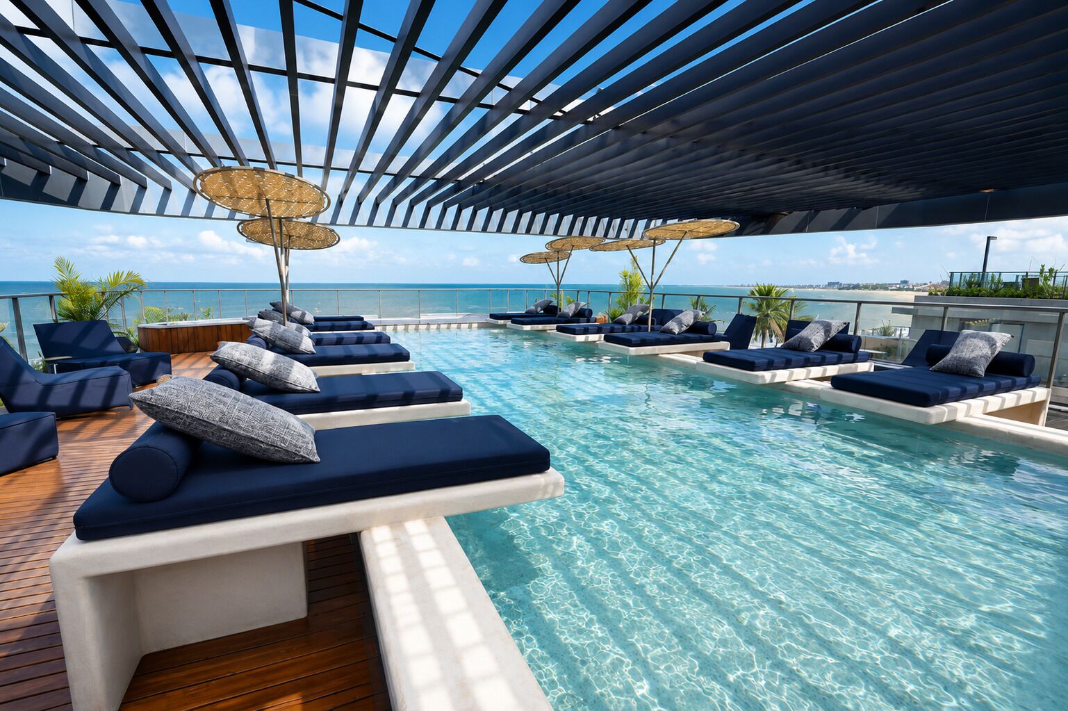 A poolside area with lounge chairs and umbrellas, overlooking a clear blue sky and water.