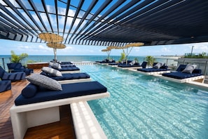 A poolside area with lounge chairs and umbrellas, overlooking a clear blue sky and water. - Nawi Beachfront Escape Apartment - Pool, Gym & Ocean Access (João Pessoa)