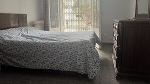 A bedroom with a bed, a dresser, a radiator, and a window with a metal gate.