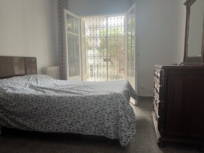 Una camera da letto con un letto, una cassettiera, un termosifone e una finestra con inferriata.