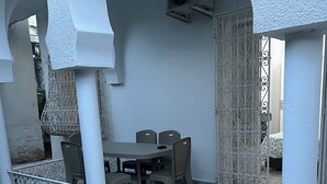 A covered outdoor seating area with a table and chairs, an air conditioning unit, and a decorative metal fence.