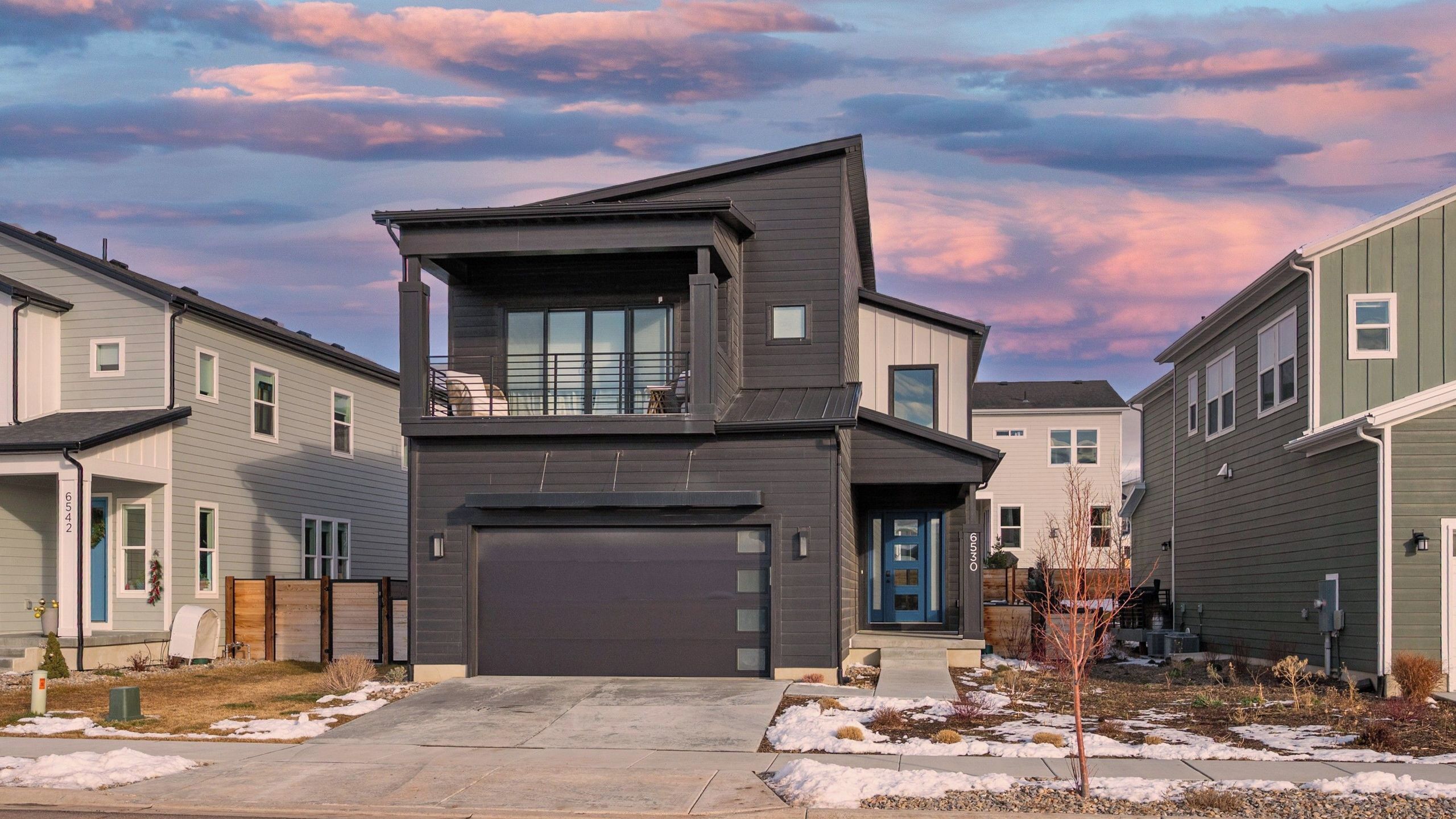 A modern two-story house with a garage, a balcony, and a view of neighboring houses.