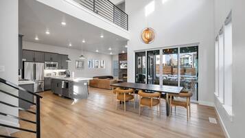 A modern kitchen with stainless steel appliances, a dining area with a wooden table and chairs, and a large window overlooking a snowy landscape.