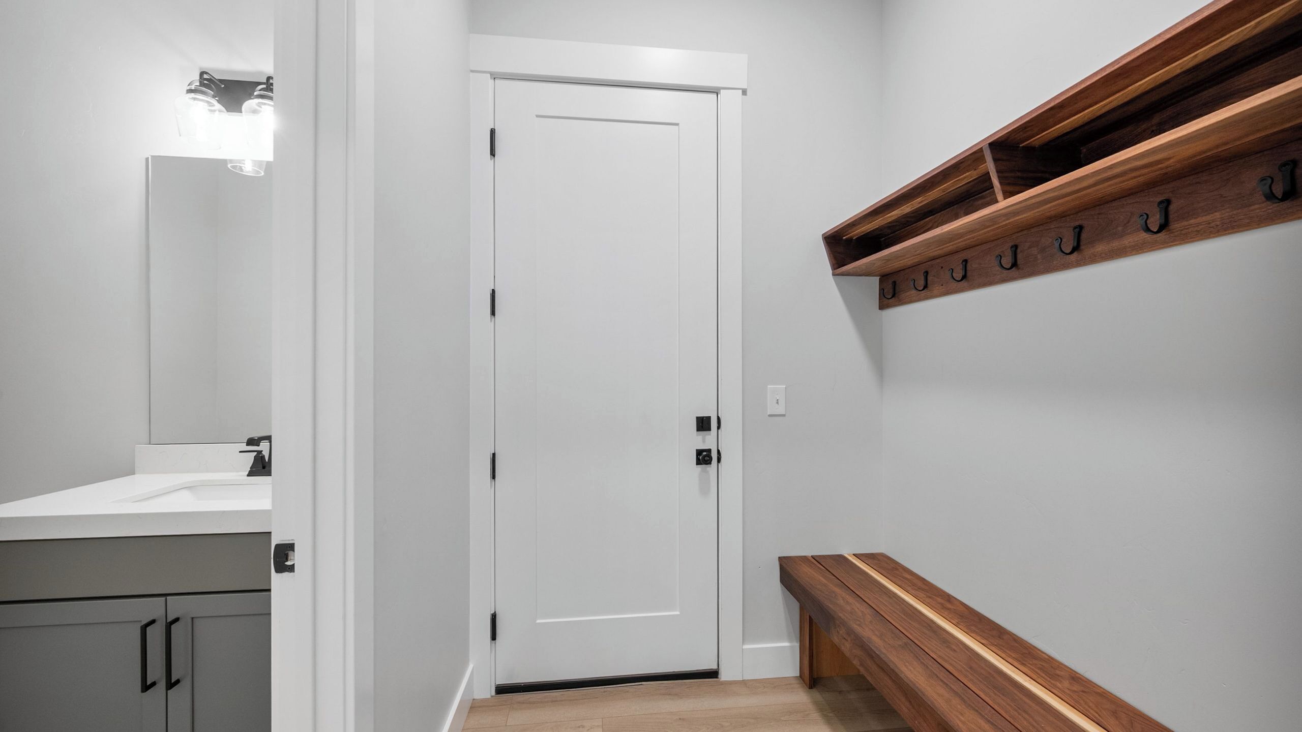 A hallway with a white door, a wooden bench, a coat rack, and a mirror.