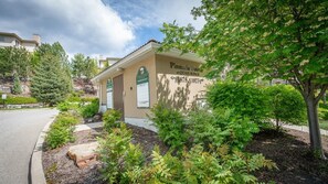 A building with a sign indicating it's for sale, surrounded by greenery and a clear sky. - Mountain View Condo | Pool, Hot Tub & Golf 2213 (Kelowna)
