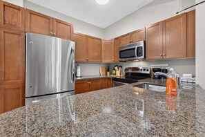 A kitchen with wooden cabinets, stainless steel appliances, granite countertops, and a stainless steel refrigerator. - Mountain View Condo | Pool, Hot Tub & Golf 2213 (Kelowna)