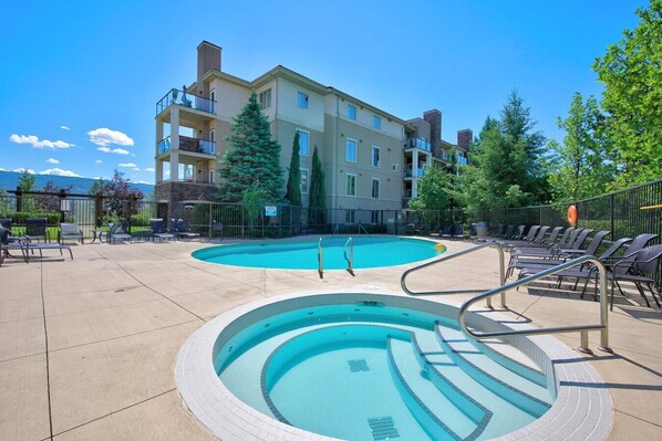 A swimming pool with steps, lounge chairs, and a building with balconies. - Mountain View Condo | Pool, Hot Tub & Golf 2213 (Kelowna)