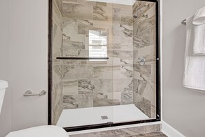 Une douche avec une porte en verre, des carreaux de marbre et une barre d’appui.