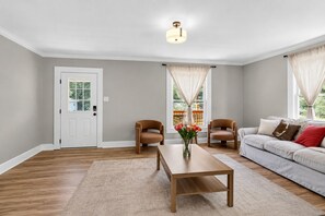 A living room with a wooden floor, a white door, two leather chairs, a beige sofa, a wooden coffee table, and a vase with flowers. - Newly Renovated Furnished Home | Ideal for Corporate & Insurance Housing (Salisbury)