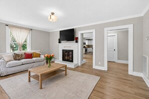A living room with a sofa, a coffee table, a fireplace, and a TV mounted on the wall. - Newly Renovated Furnished Home | Ideal for Corporate & Insurance Housing (Salisbury)