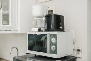 Una kitchenette compacta con microondas, cafetera y un refrigerador pequeño.