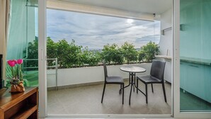 Un balcón con mesa y sillas, vistas al verdor y un cielo despejado.