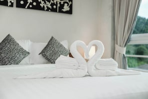 A bed with white linens, two heart-shaped towels, patterned pillows, and a window with a view.