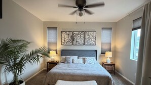 Un dormitorio con una cama grande, ventilador de techo, planta en maceta y cuadros en la pared.