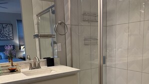 Un baño moderno con cabina de ducha de vidrio, tocador con lavamanos y espejo.