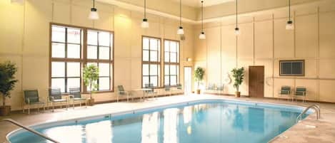 An indoor swimming pool with clear water, surrounded by chairs and potted plants.