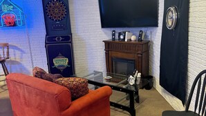 Een kamer met een flatscreen-televisie, dartbord en een open haard.