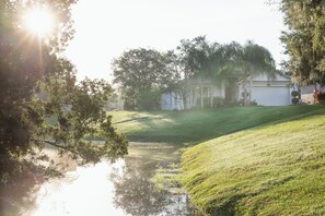 Ein Wohnhaus mit Rasen, Teich und einer weißen Villa mit Garage.
