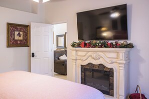 Ein Schlafzimmer mit Kamin, einem darüber hängenden Fernseher und einer Tür zu einem anderen Raum.